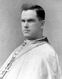 Black and white portrait of a Catholic clergyman in traditional vestments. He has short dark hair and a serious expression, looking slightly to the side. The photo has an old, historical appearance.