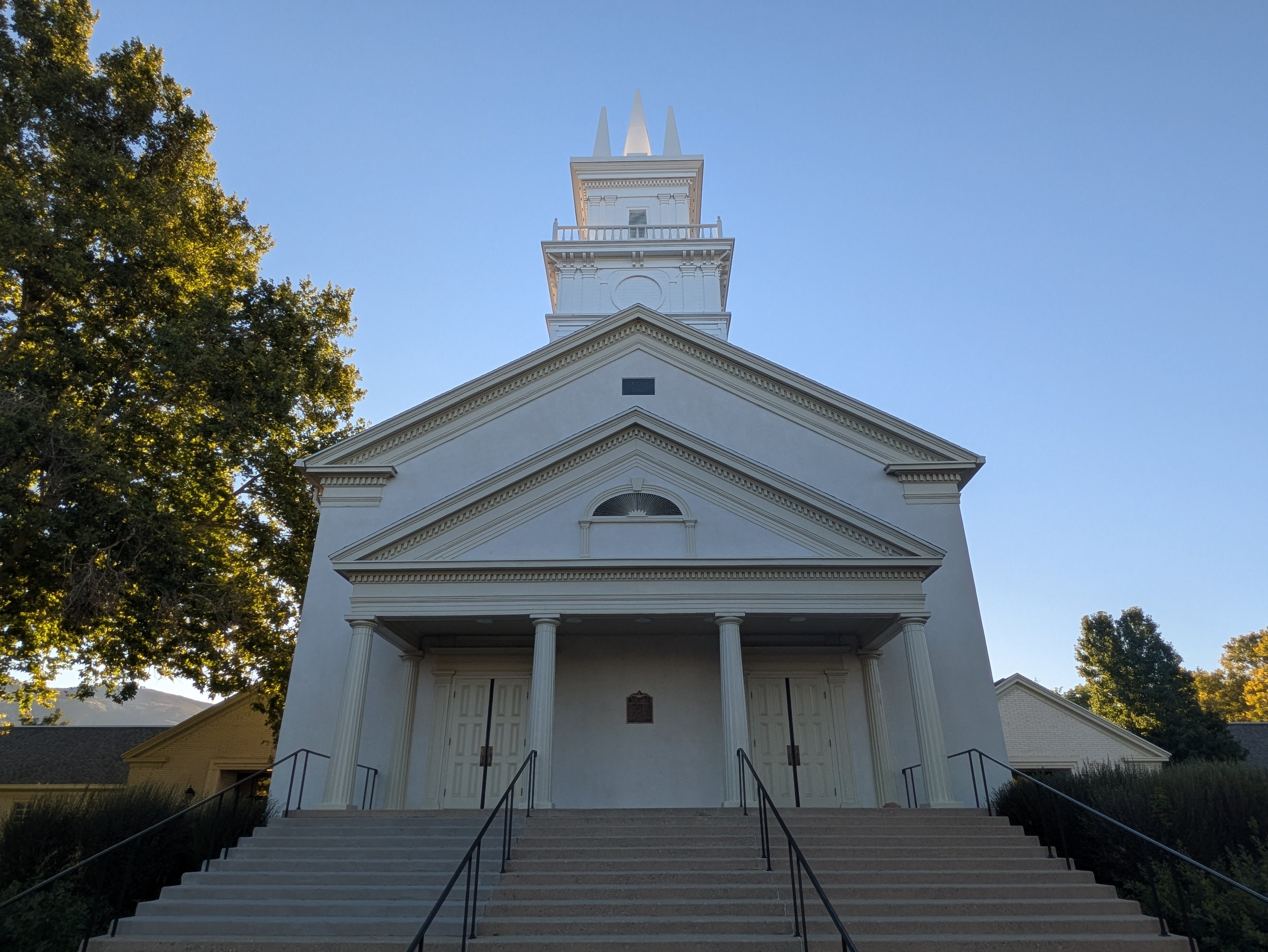 Front view of the Bountiful Tabernacle in Utah, a historic Latter-day Saint meetinghouse with white plaster exterior, classical columns, and a tall central steeple.