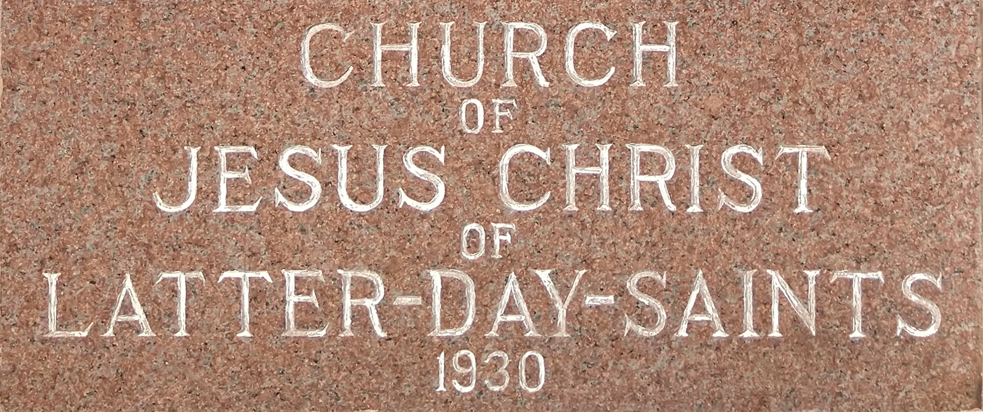 Engraved stone inscription on a red granite plaque reading 'Church of Jesus Christ of Latter-Day-Saints 1930,' with text in all capital letters except for the word 'of,' marking a 1930 meetinghouse in El Paso, Texas.