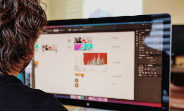 Vista da dietro le spalle di un uomo che lavora alla grafica di un sito web al computer.