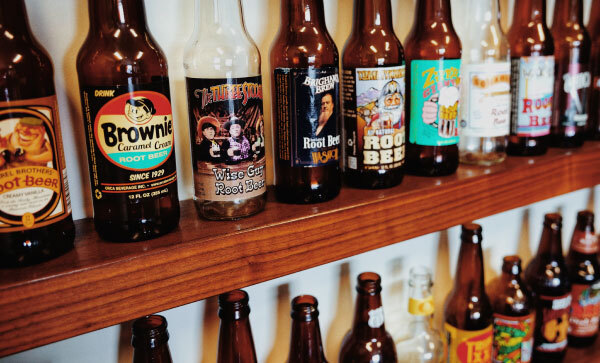 Des étagères murales en bois avec des rangées de différentes bouteilles de root beer gourmet.