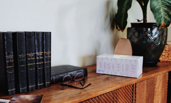 Delen van "A Contemporary History of The Church", een bril, een tissuebox en een potplant boven op een houten kast.