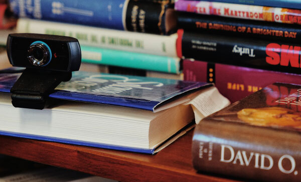 Primo piano di un tavolo coperto di libri sul mormonismo, uno dei quali usato come supporto per una webcam.