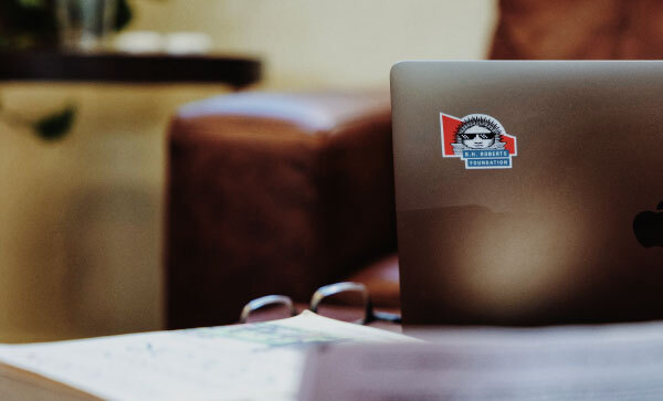 Geöffneter Laptop zeigt einen Aufkleber mit dem Logo der B. H. Roberts Foundation, auf dem ein Nauvoo Sunstone mit Sonnenbrille zu sehen ist.