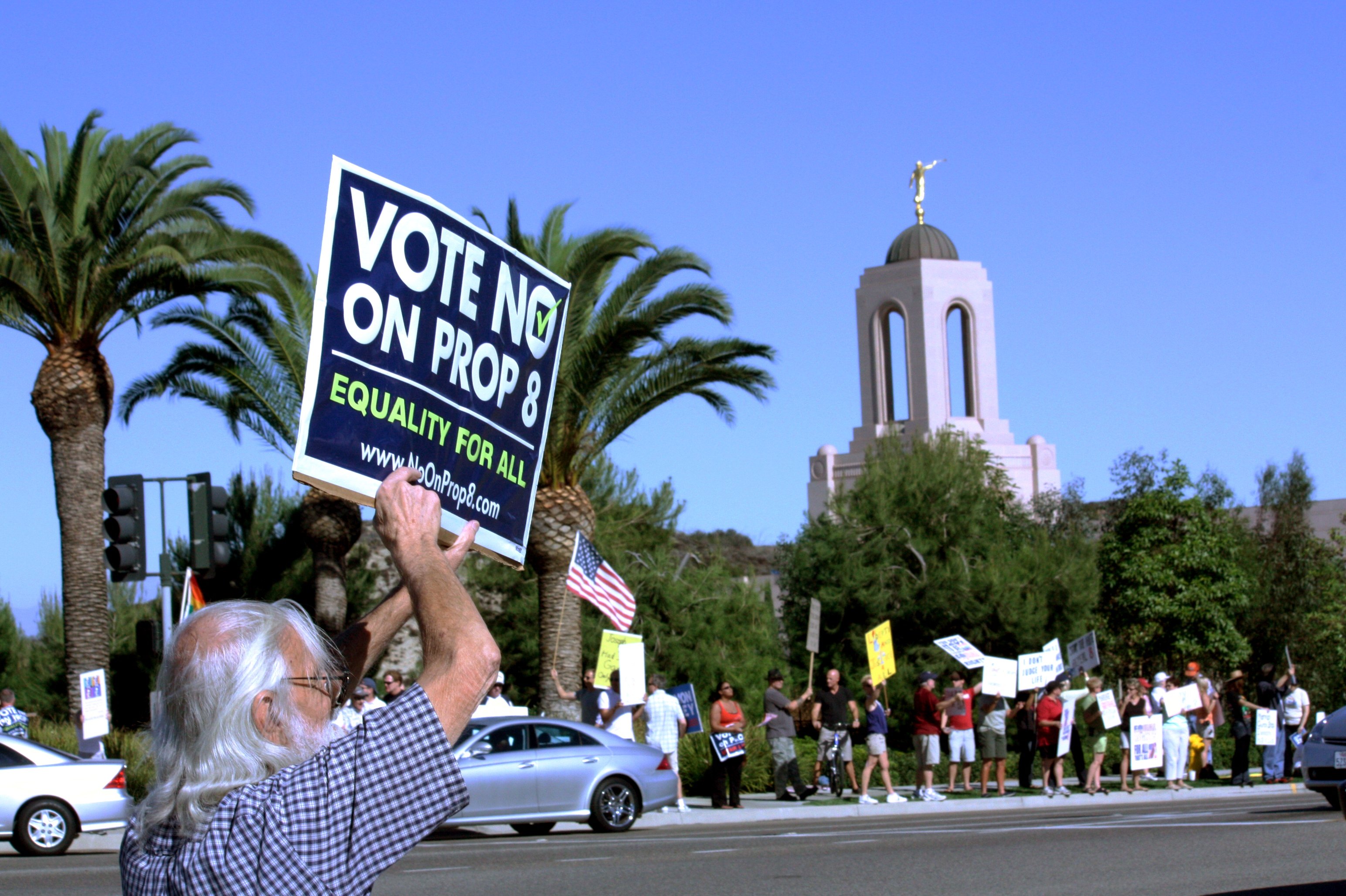 白髪の男性が、カリフォルニア州のLDSニューポート神殿の外で、「prop 8に反対票を―すべての人に平等を」と書かれた看板を持っています。