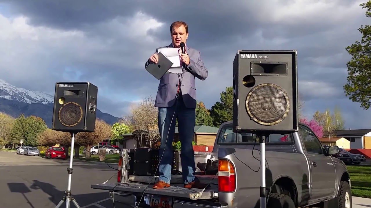Een kleurenfoto van 26 april 2016 van Jeremy Runnells, auteur van de CES Letter, waarop hij aankondigt dat hij de Kerk van Jezus Christus van de Heiligen der Laatste Dagen verlaat, staand op de achterklep van een pick-uptruck, met PA-luidsprekers aan beide kanten, op een parkeerplaats van een kerk, met bergen op de achtergrond.
